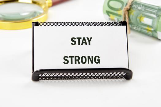 A small sign displays the uplifting message stay strong set against a backdrop of money and a magnifying glass, symbolizing determination and focus in challenging times photo