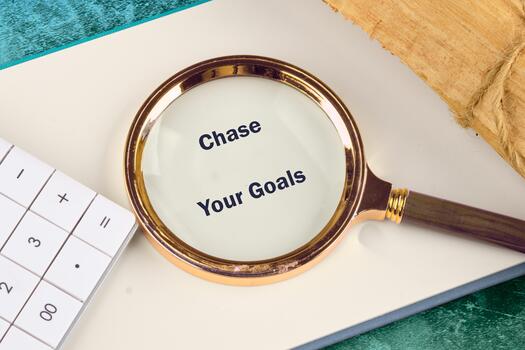A motivational scene featuring a magnifying glass over a notebook with the phrase Chase Your Goals prominently displayed. The setup encourages focus and determination photo