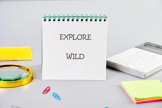 A notepad opens to the words explore wild, surrounded by colorful sticky notes, paper clips, and a magnifying glass, inviting creativity and adventure in a lively workspace photo