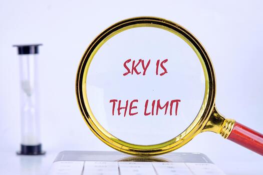 A magnifying glass focuses on the words sky is the limit, symbolizing ambition and potential. In the background, an hourglass rests, representing the value of time in achieving goals photo
