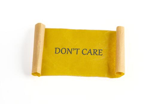 A yellow scroll displays a message in gray letters. It reads DONT CARE and rests on a white background. The scroll is rolled at both ends in a light brown color photo