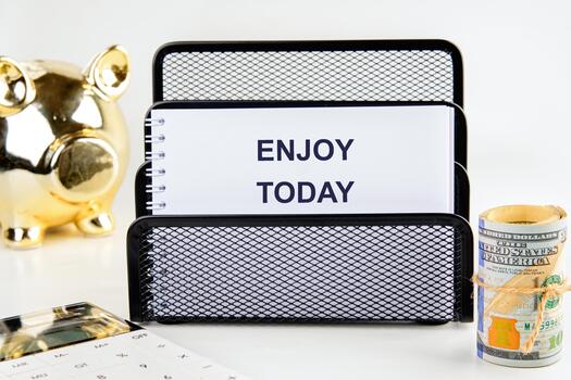 A notepad reading ENJOY TODAY sits in a black wire organizer, next to a piggy bank and rolled-up money with a calculator sitting at the bottom left photo