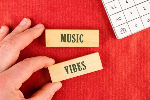 A person holds wooden blocks with the words Music and Vibes on a red background. A calculator sits in the corner, possibly calculating the sounds frequency photo