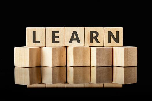 Wooden blocks with letters spelling LEARN are stacked on a reflective surface against a black backdrop, emphasizing the concept of gaining knowledge photo
