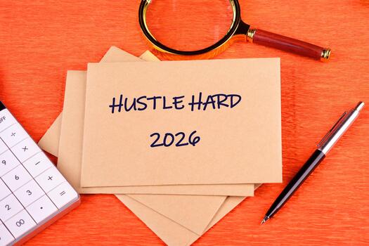 A note card shows Hustle Hard 2026 near a calculator, pen, and magnifying glass. This conveys a message about strategizing and planning for success in the future photo