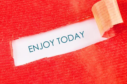 Red textured paper is torn open, revealing a message that reads ENJOY TODAY. A reminder to embrace the present and appreciate the little things photo