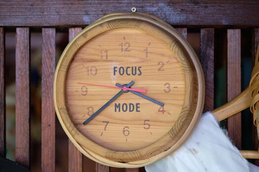 A round wooden clock hangs on a wooden wall. The clock face says FOCUS MODE instead of numbers. The clocks hands indicate a specific time photo