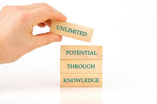 A hand carefully places a wooden block labeled unlimited on a stack of blocks that spell out potential through knowledge, symbolizing growth and learning photo
