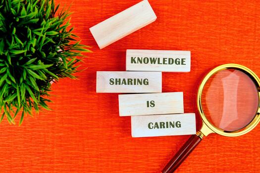 On a bright orange surface, wooden blocks are arranged to convey the message knowledge sharing is caring, accompanied by a magnifying glass and a small green plant for added visual interest photo