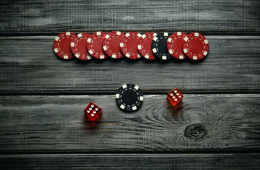 A collection of red and black poker chips is neatly arranged on a rustic wooden table alongside two red dice. This setup highlights an exciting game night atmosphere photo