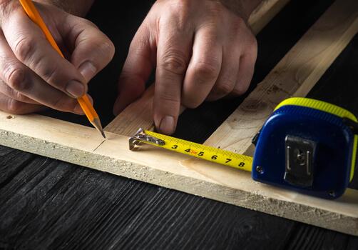 A carpenter makes pencil marks on a block of wood. Hands of the master close-up at work. Working environment in a carpentry workshop. photo