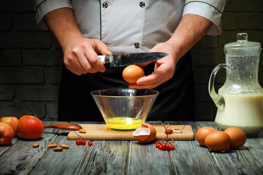 A chef cracks open eggs into a glass bowl while chopping apples on a wooden surface. Nearby are milk, nuts, and berries, creating a fresh cooking scene during the evening photo