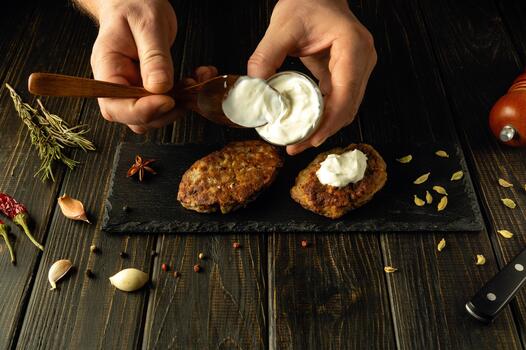 Close-up of a chef hands using a spoon adding sour cream to fried cutlets on a sorting board. The concept of preparing delicious food in a hotel photo