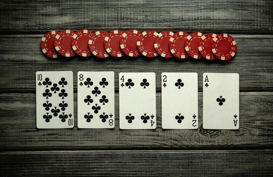A playful gathering features five playing cards displayed face up alongside a stack of red poker chips on a rustic wooden table. Friends enjoy their time together while playing photo