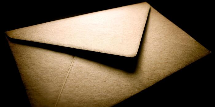 A textured brown envelope with a closed flap is dramatically lit against a dark background creating a mysterious mood photo