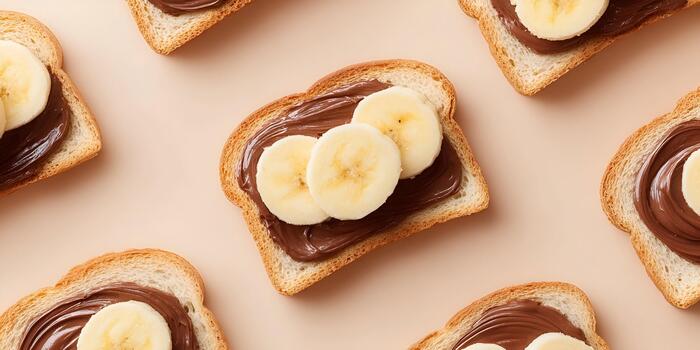 An overhead view displays multiple slices of toast spread with chocolate and topped with fresh banana slices on a light background photo