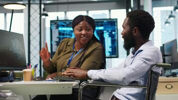 puesta en marcha oficina ingeniero en silla de ruedas hablando con colega, desarrollando artificial inteligencia modelos eso especialista con paraplejía y compañero de trabajo corriendo simulaciones para ai pronóstico, cámara un video