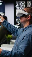 vertical masculino ingeniero utilizando vr auriculares y ai en interior diseño software a puesto de trabajo, Moviente bienes para Departamento diseño con artificial inteligencia sugerencias en 3d hacer programa. cámara b. video