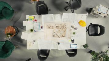 Top down view zoom in of developers and architects in business meeting reviewing blueprints and structural designs. Team discusses redevelopment and city planning for housing growth. Camera A. video