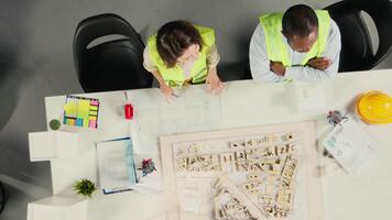 topp ner se av utvecklare i modern kontor miljö planera konstruktion. arkitekter och ingenjörer diskutera webbplats förberedelse, bemästra planen uppdateringar och verklig egendom investering. kamera a. video