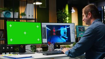 croma chiave con maschio dipendente Lavorando su gioco sviluppo, utilizzando doppio monitor a postazione di lavoro. giovane esperto ingegnere la creazione di futuristico navicella spaziale stazione su moderno Software. telecamera b. video
