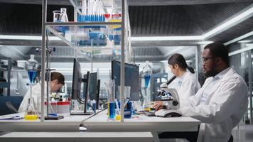 Lab microbiologist using scientific microscope for cellular analysis, writing down information. Research facility expert using optical device gear to examine medical samples, taking notes, camera A video