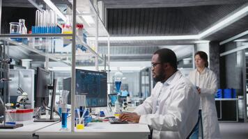 clínico microbiólogo en laboratorio mirando a sangre muestra en prueba tubo, utilizando ordenador personal software. médico investigación experto utilizando computadora programa a analizar optimista fluido muestra en frasco, cámara un video