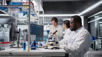 ricercatore operativo microscopio, fare campione osservazioni nel laboratorio, scrittura Appunti. scienziato studi fazzoletto di carta sotto ottico dispositivo nel biotecnologia laboratorio, segnalazione risultati, telecamera un' video