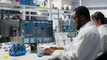 histologi tekniker använder sig av pipett till extrahera reagens från glas in i testa rör på laboratorium bänk. forskning anläggning arbetstagare på pc skrivbord gör pipettering procedur med droppare, kamera b video