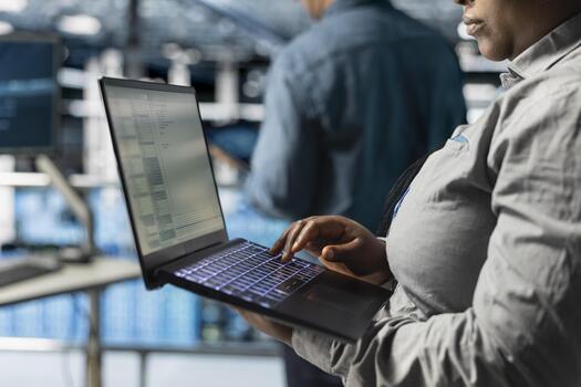 Close up of server room coworkers deploying new builds to improve uptime using software on laptop. Team of data center programmers writing code for resource optimization using notebook photo