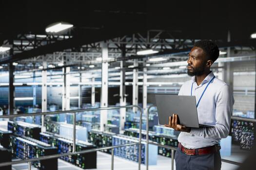 Server hub employee visualizing large language AI model using laptop, overseeing server room infrastructure from industrial platform. Data center technician reviews neural network. photo
