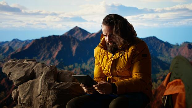 Male hiker struggles to work online in windy conditions on a remote mountain peak. Battling weak signals and cold weather, explorer is obsessed with technology and the internet. Camera A. photo