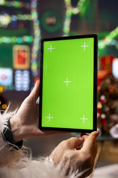Close up of Santa Claus using mockup tablet in North Pole workshop to read letters from kids. Saint Nicholas answering online messages from children using green screen touchscreen device photo