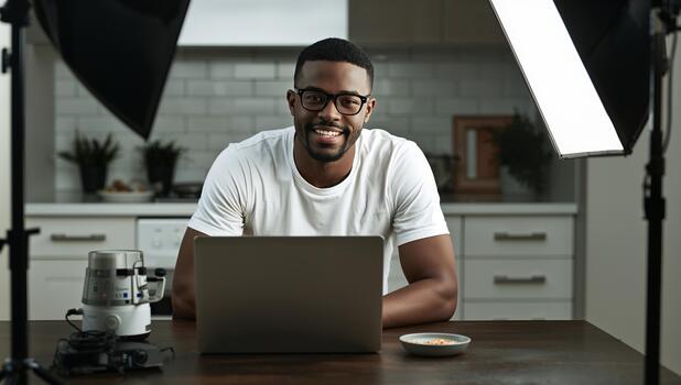 Young Man Smiling While Working on a Laptop in a Modern Kitchen During Daylight Hours photo