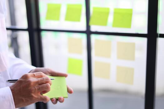 Businessman putting notes on mirror for organizing thoughts, planning tasks for project management and brainstorming. photo