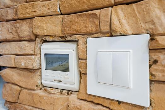 device inspection imagery, inspecting home heating system with illuminated controls on stone surface, detailed examination of electronic thermostat and sensor set against textured stone backdrop photo