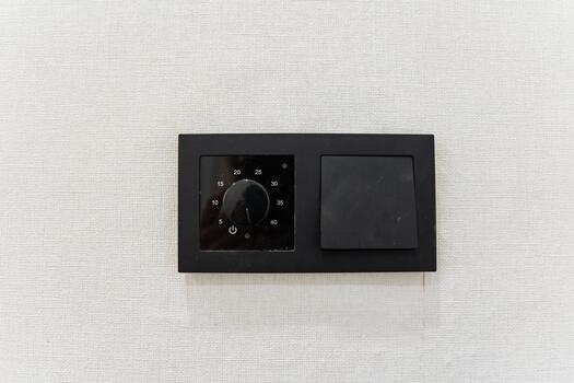 wallmounted thermostat device, beige textured wallpaper with minimalistic thermostat, minimalist indoor environment featuring wallmounted heater control with touch interface and textured background photo