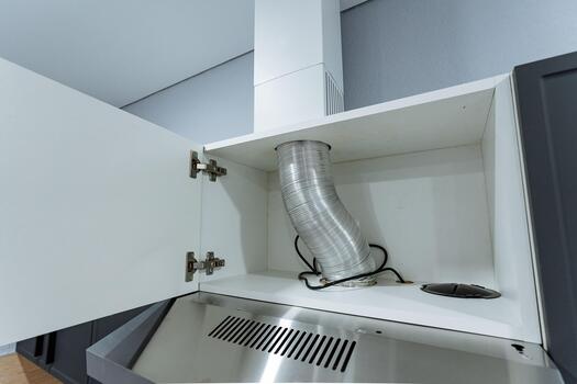 vent connection above stainless range hood, renovation context shows exposed duct and open cabinetry, maintenance scenario with visible hinge hardware and flexible vent connection photo