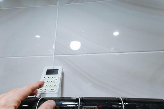 hand operating wall mounted controller, technician interacting with keypad, braided hose and chrome rail visible, hands on maintenance check, tactile adjustment during service, focused closeup. photo