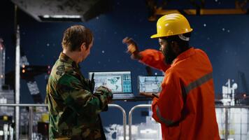 Security officer in camouflage uniform monitors offshore drilling operation, using radio communication for intelligence coordination and threat detection in maritime environments. Camera B. video