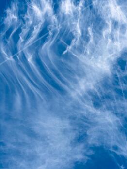 Whispers of the sky dance in a serene blue canvas during a bright afternoon, showcasing nature's artful display of clouds and their soft, flowing patterns photo