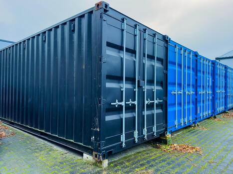 Colorful shipping containers lined up in a storage area during an overcast day, showcasing different textures and hues while surrounded by greenery photo