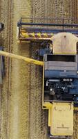 Top view on agricultural machinery. Combine harvester pouring out grains into the trailer of a tractor on the field background. Motion camera bottom up. Vertical video