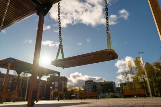Wooden swing hanging from a sturdy frame in a sunny park, surrounded by trees and buildings, creating a serene atmosphere for relaxation and play photo
