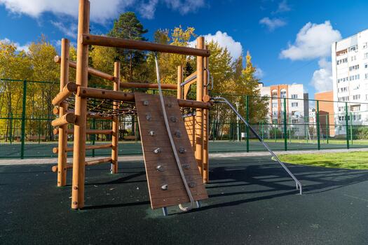 Wooden playground structure with climbing wall and slide, surrounded by green grass and trees, under a bright blue sky with fluffy clouds, inviting outdoor play and exploration photo