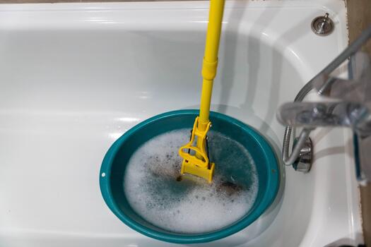 Cleaning tool submerged in a turquoise basin filled with soapy water, showcasing the process of maintaining hygiene in a bathroom environment with copy space photo