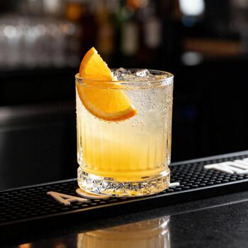 Refreshing citrus cocktail with ice sits on a damp bar mat against a dark background photo