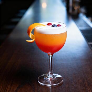 vibrante en capas cóctel adornado con agrios giro y Fresco bayas descansa en un oscuro de madera bar parte superior foto