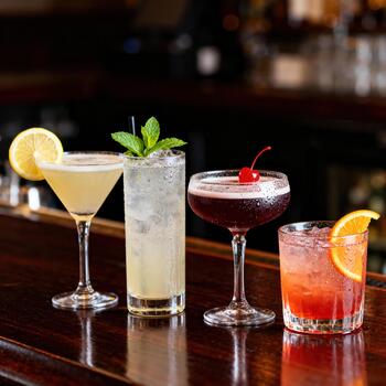 Assortment of four refreshing mixed drinks displayed upon a polished wooden bar surface photo