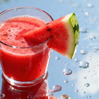 Glass filled with vibrant red fruit beverage garnished with a fresh wedge sitting on a reflective surface. photo